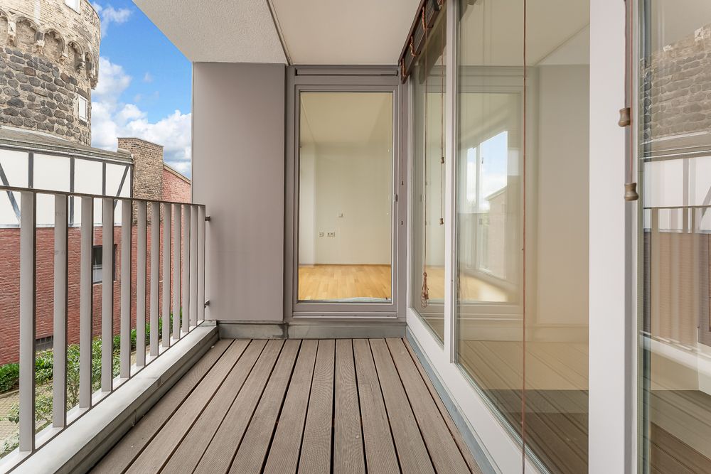 Balkon mit Holzboden und Glasfront, Blick in einen leeren Raum mit Parkettboden.