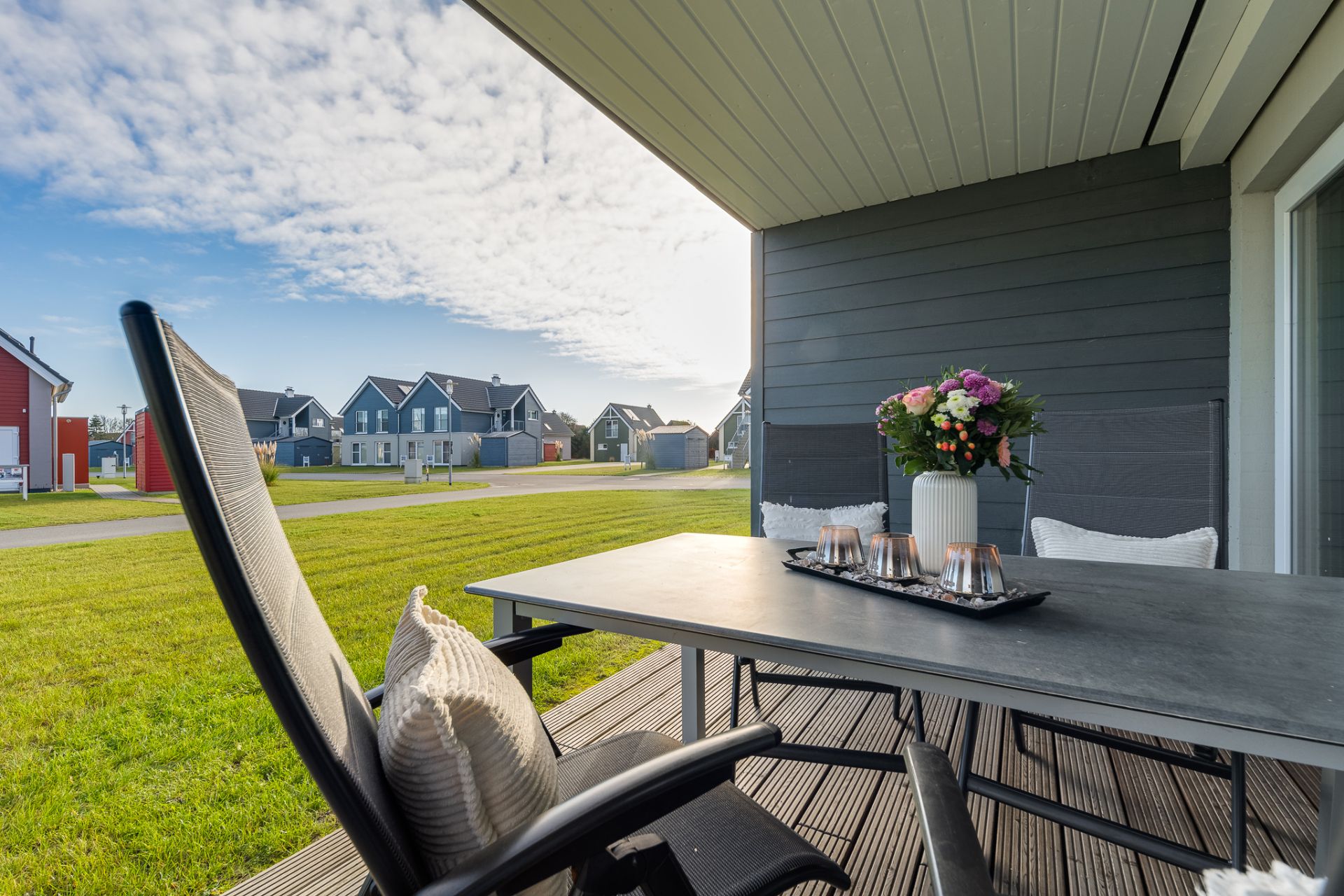 Überdachte Terrasse mit Tisch, Stühlen und Blumen, Blick auf Rasen und benachbarte Häuser.