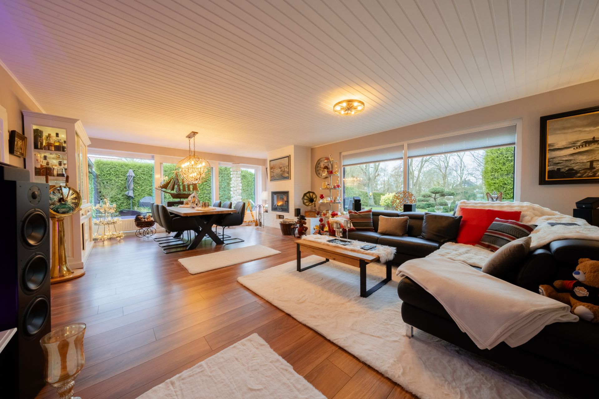 Helles Wohnzimmer mit Sofa, Essbereich, großen Fenstern und Holzboden, Blick auf Garten.