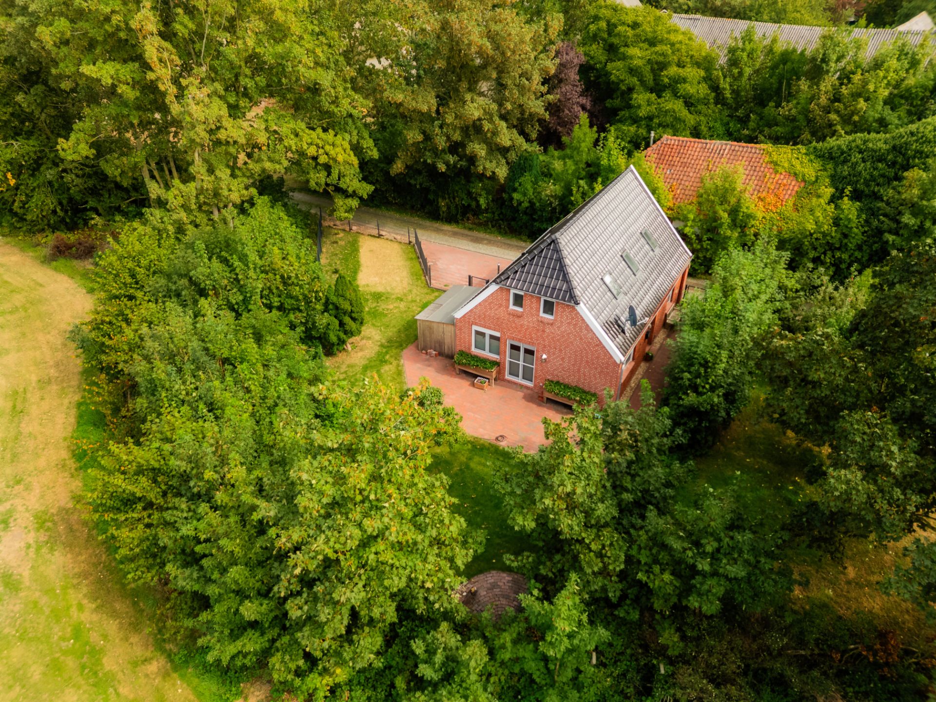Luftaufnahme eines roten Einfamilienhauses mit Garten, umgeben von vielen Bäumen.