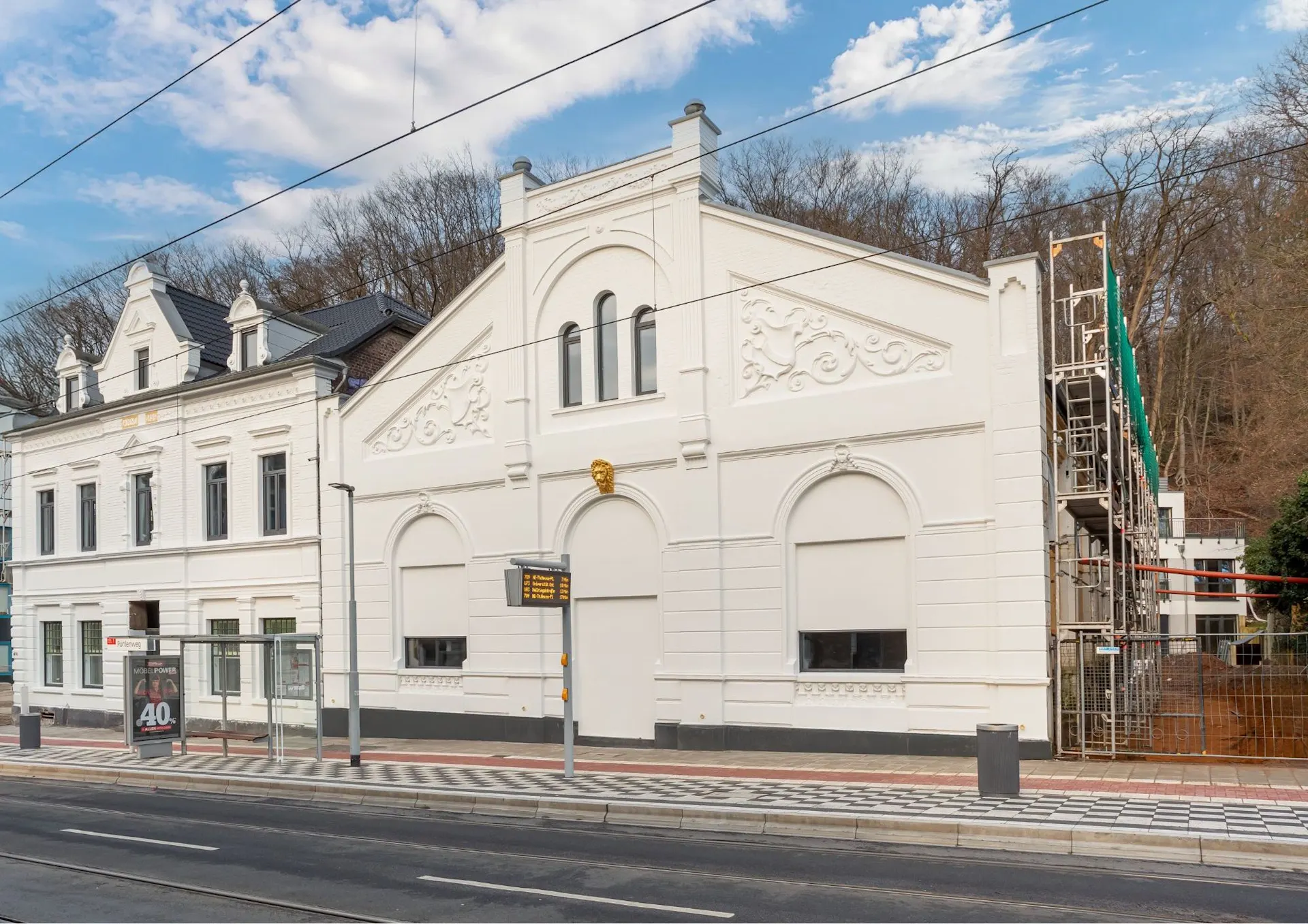 Zwei weiße Wohngebäude mit verzierten Fassaden an einer Straßenbahnhaltestelle.