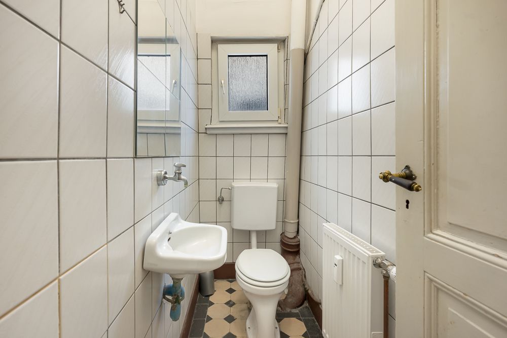 Kleines Badezimmer mit Toilette, Waschbecken, Fenster und weißen Fliesen.