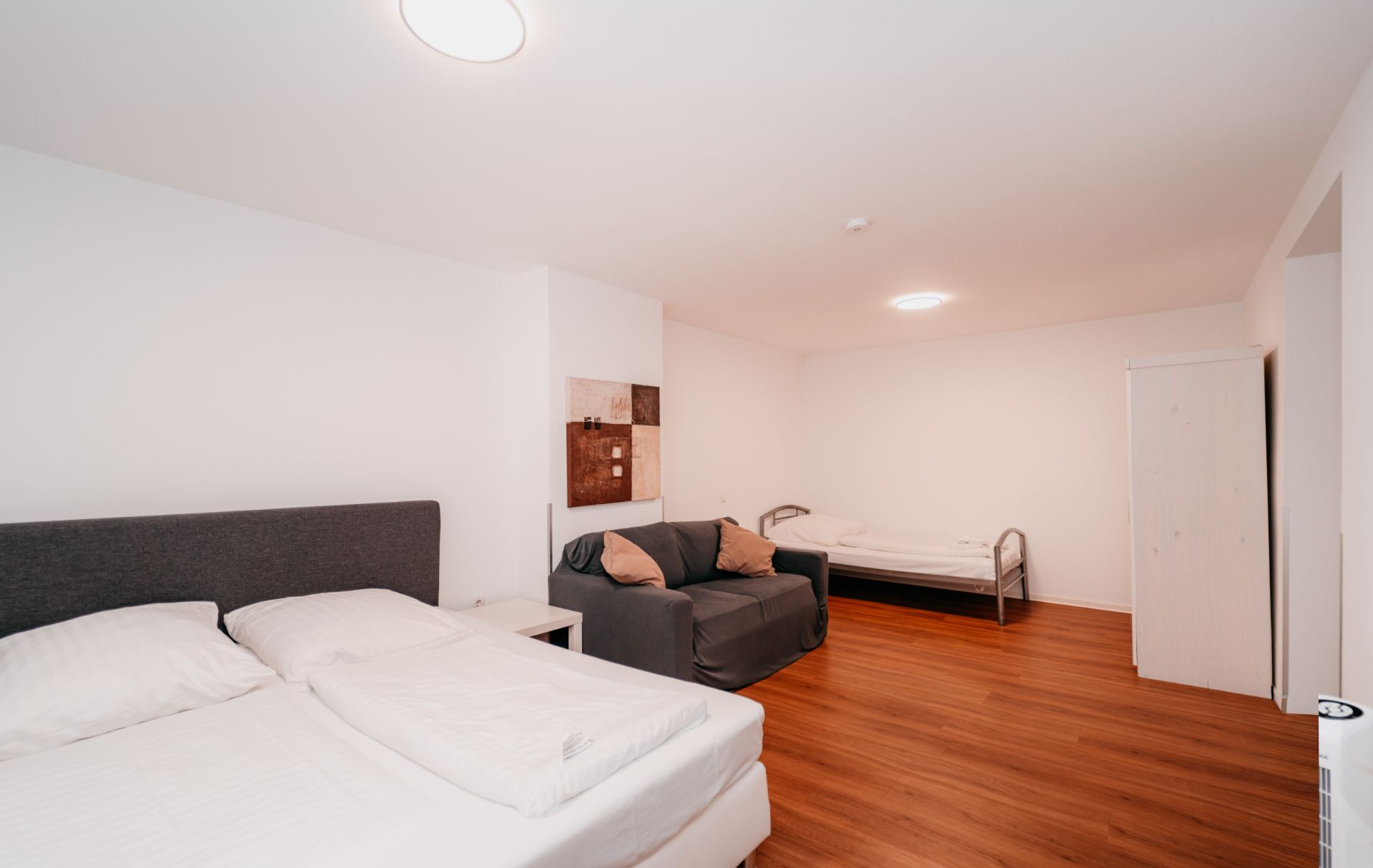 Helles Schlafzimmer mit Doppelbett, Schlafsofa, Einzelbett, Holzfußboden und Schrank.