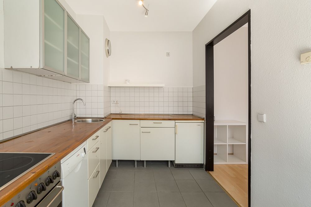 Helle Küche mit weißen Schränken, Holzarplatte und Fliesen an der Wand.