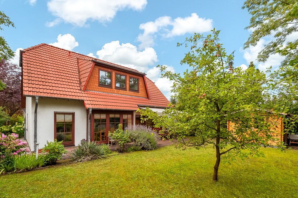 Haus mit rotem Dach und großem Garten mit Bäumen und Blumenbeeten.