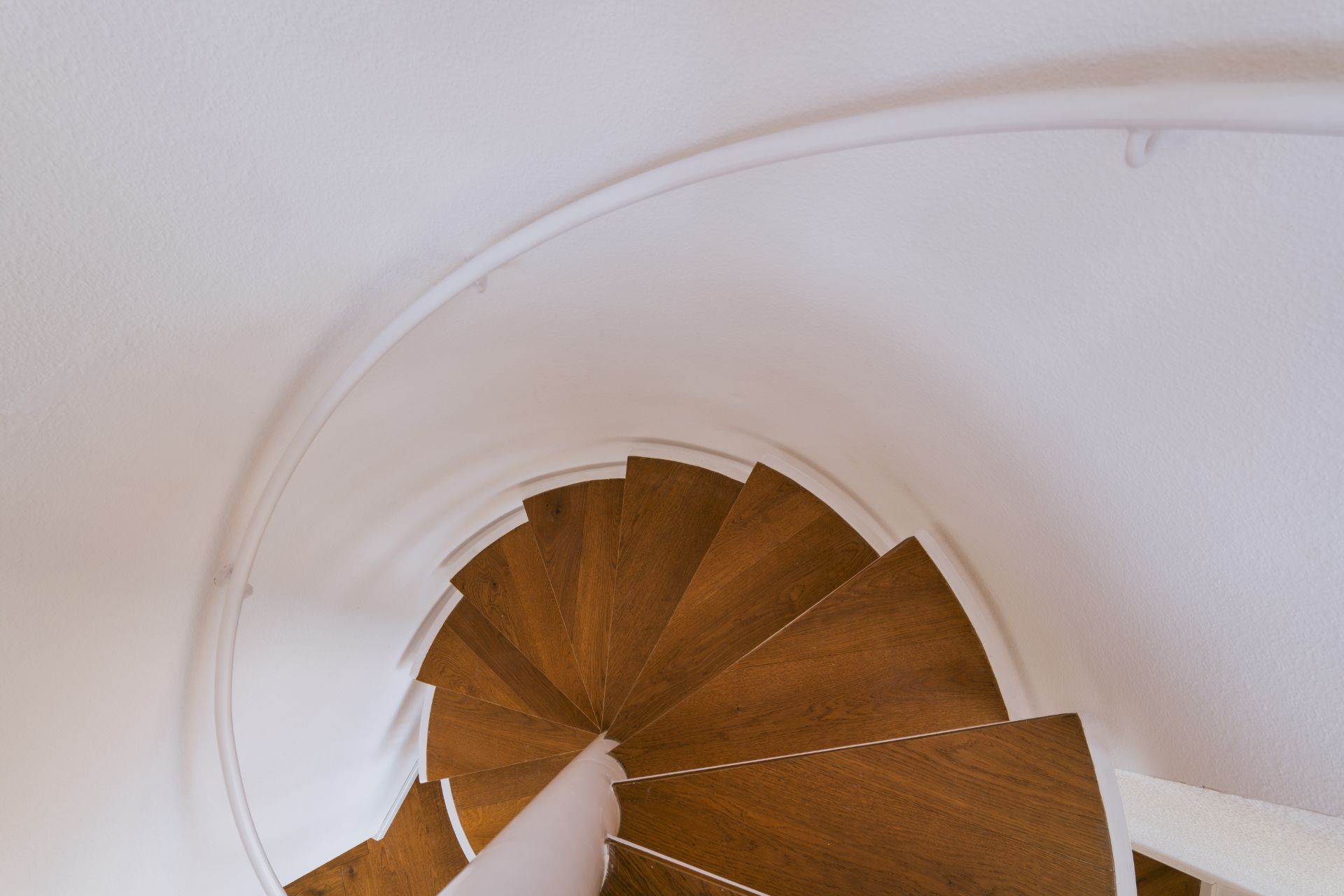 Holztreppe in einer Wendeltreppe mit weißem Geländer, von oben fotografiert.