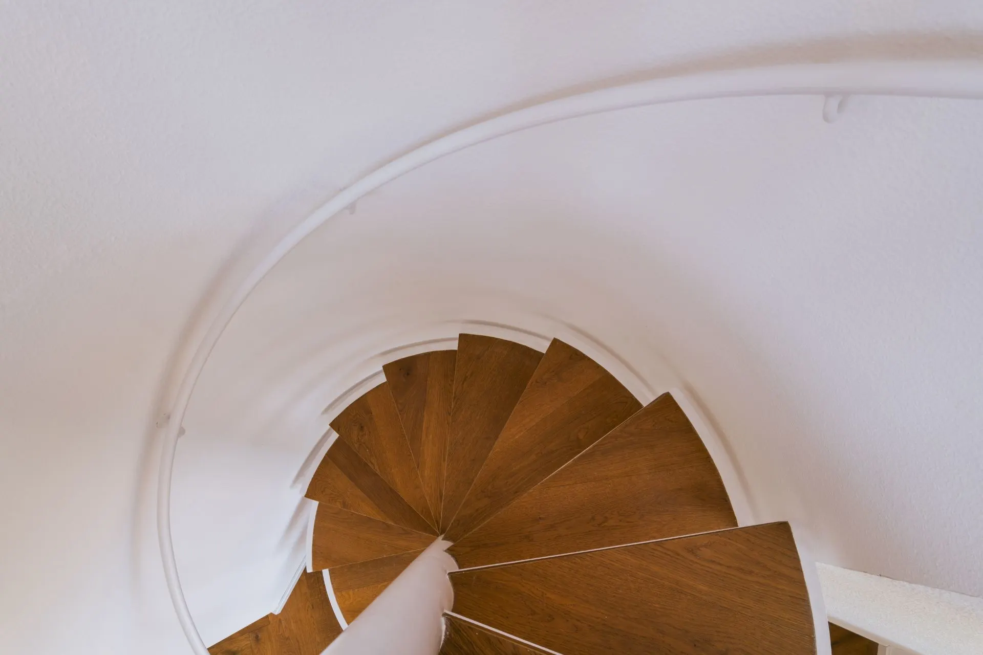 Holztreppe in einer Wendeltreppe mit weißem Geländer, von oben fotografiert.