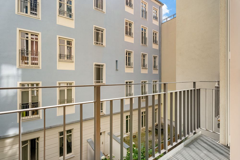 Blick von einem Balkon auf einen Innenhof mit hellblauer Hausfassade und mehreren Fenstern.