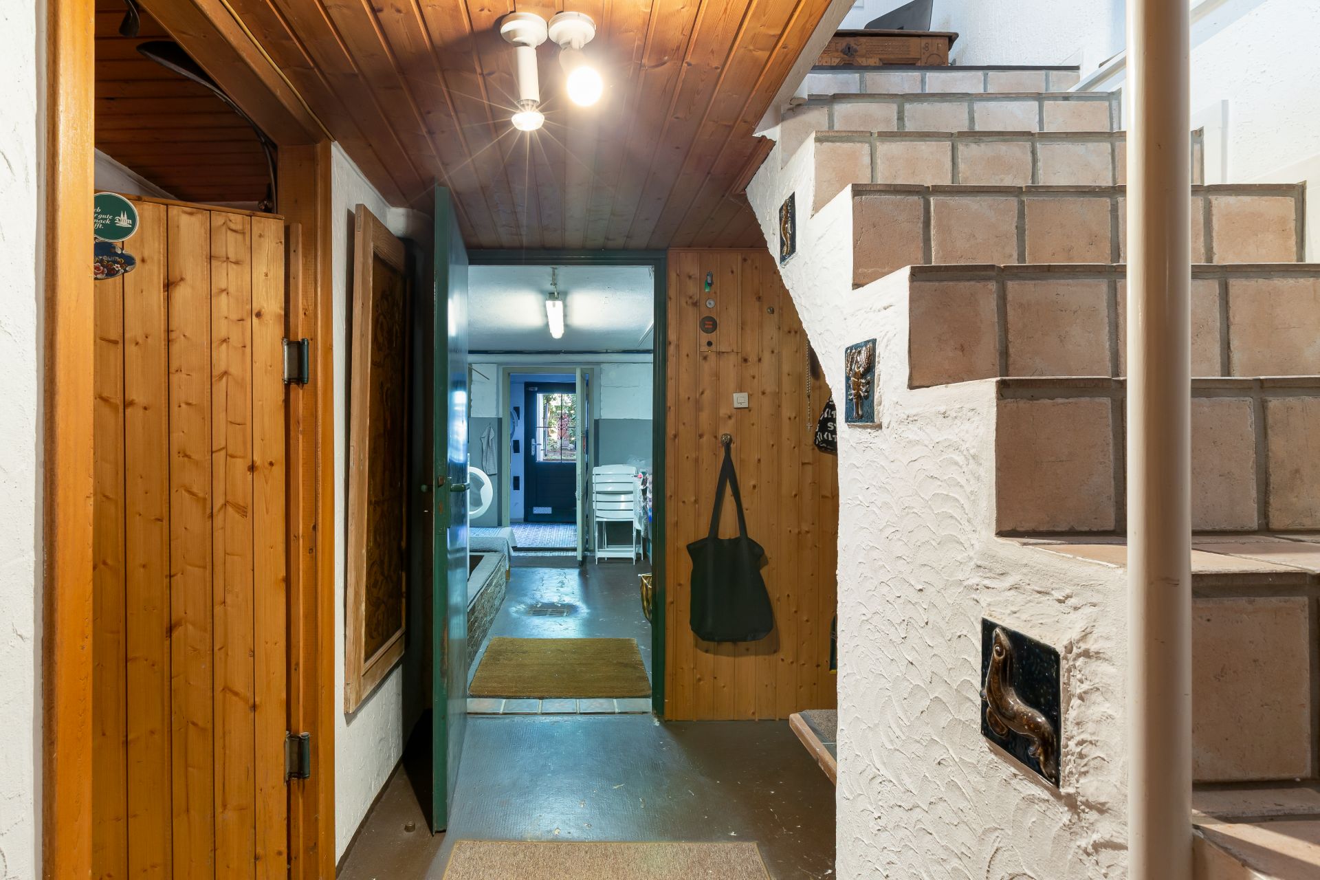 Flur mit Holzwänden und Decke, offene Tür, Treppe mit Fliesen, Blick in weiteren Raum.