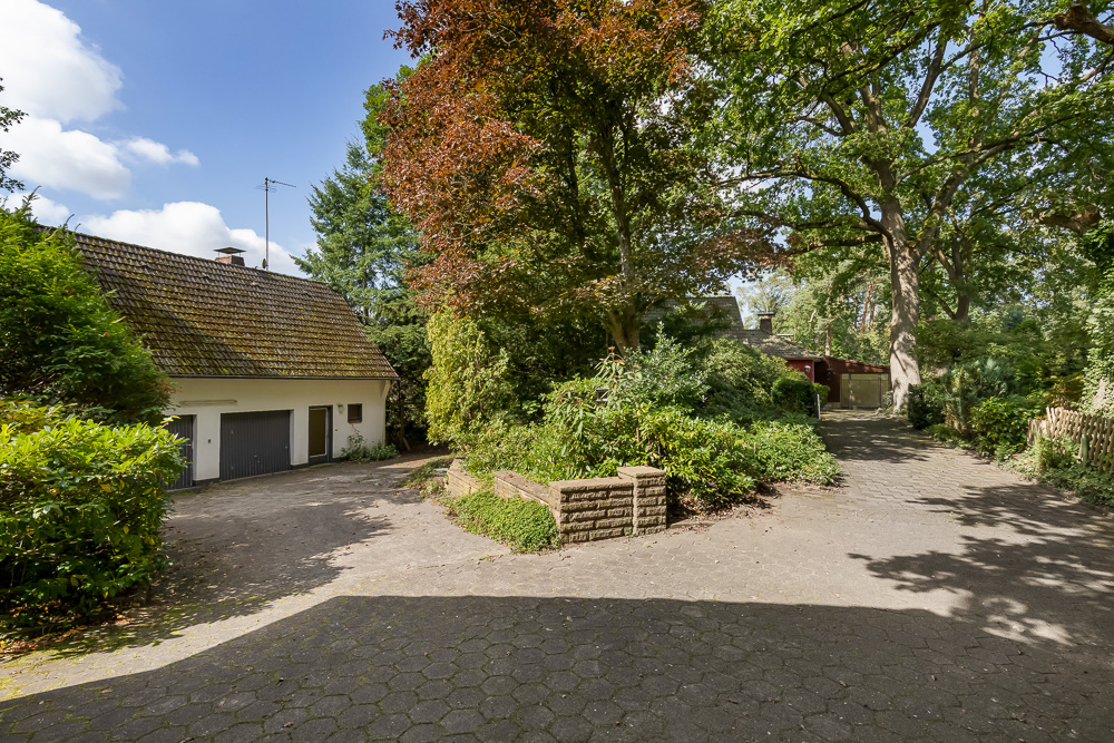 Einfamilienhaus mit Doppelgarage, Auffahrt und umgeben von vielen Bäumen und Sträuchern.