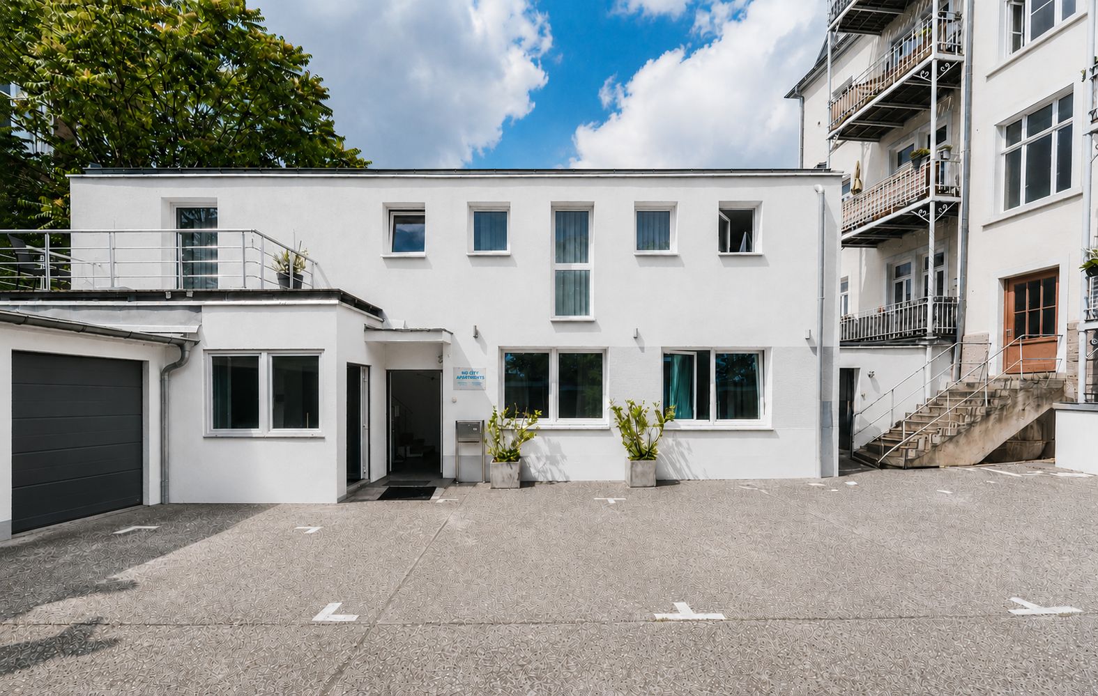 Weißes Wohngebäude mit mehreren Fenstern und Parkplatz davor.