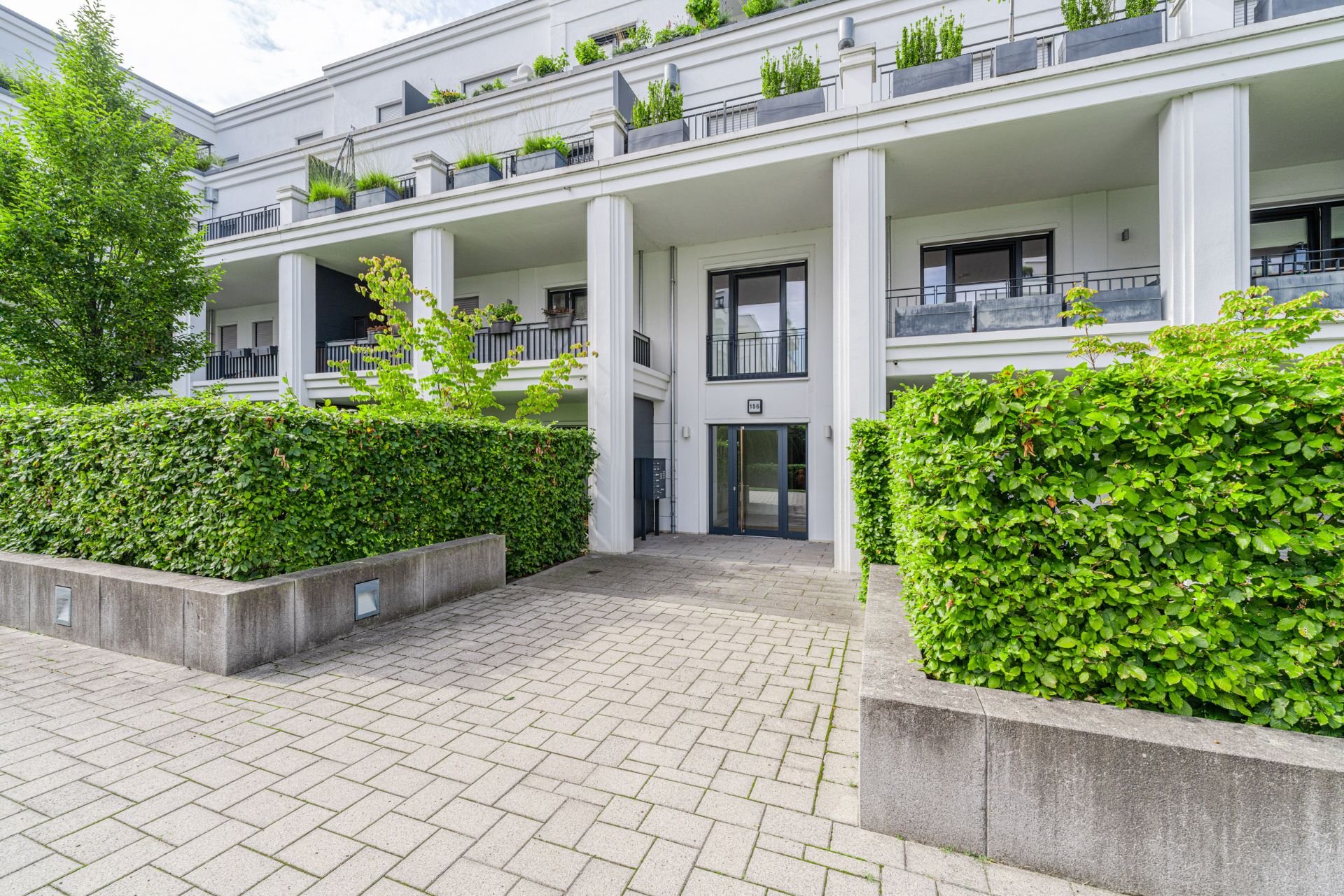 Moderner Wohnungseingang mit großen Säulen, Balkonen und viel Grün.