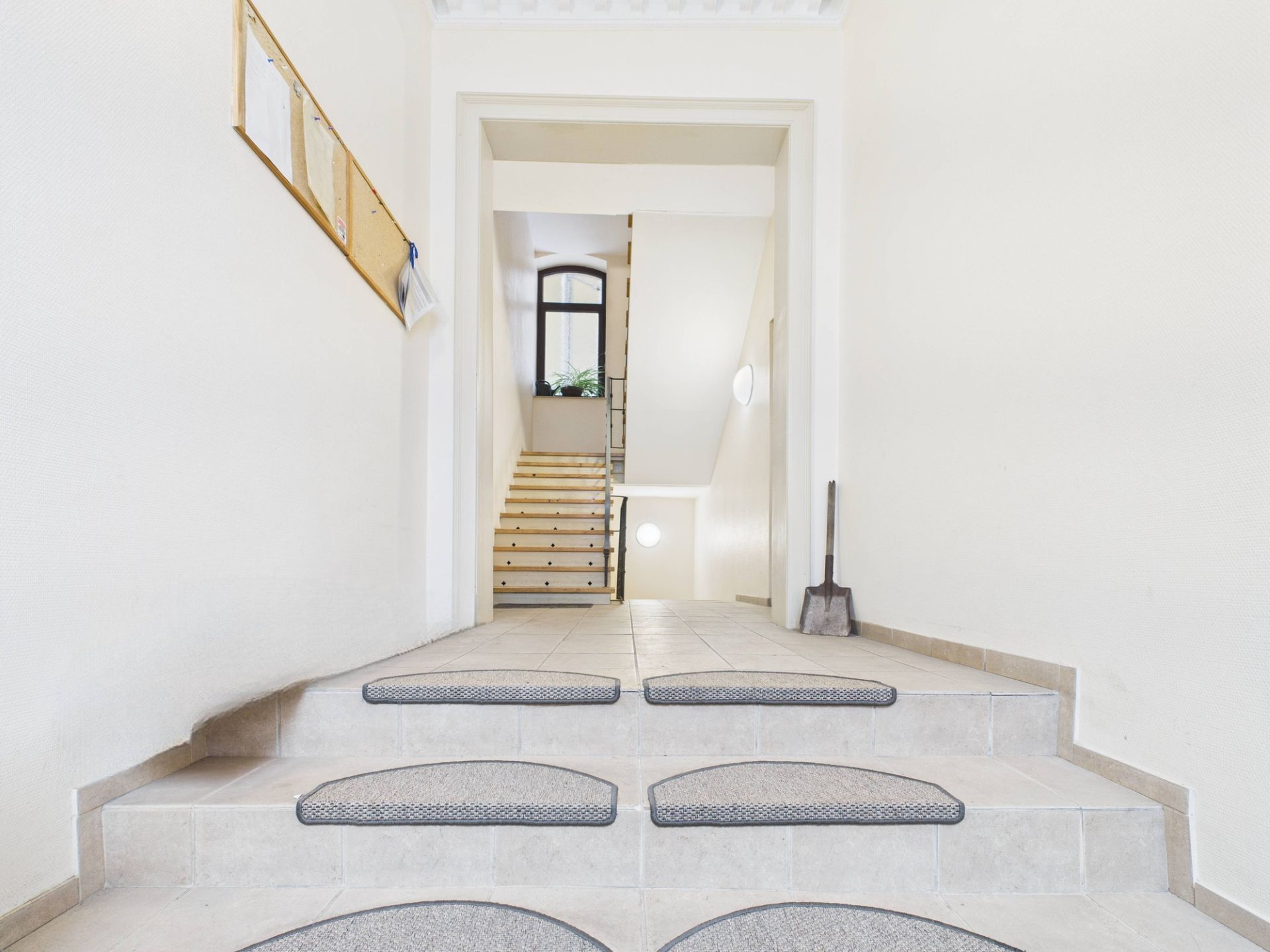 Heller Hausflur mit Stufen, Treppe und einem Fenster im Hintergrund.