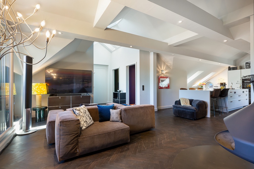 Modernes Wohnzimmer mit braunem Sofa, großem Fernseher und offener Küche im Hintergrund.