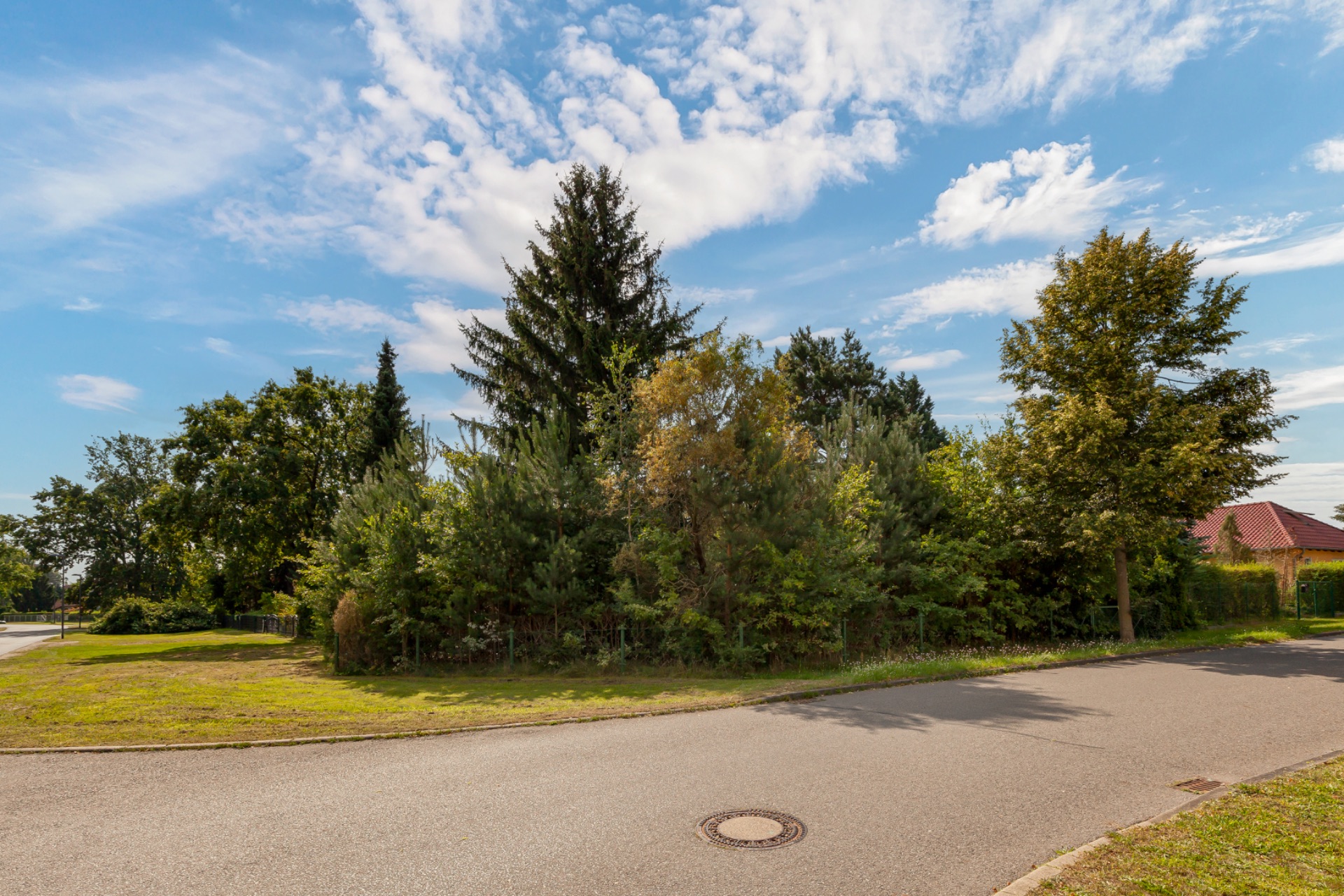 Straße mit Gehweg, grünen Bäumen und blauem Himmel mit Wolken.