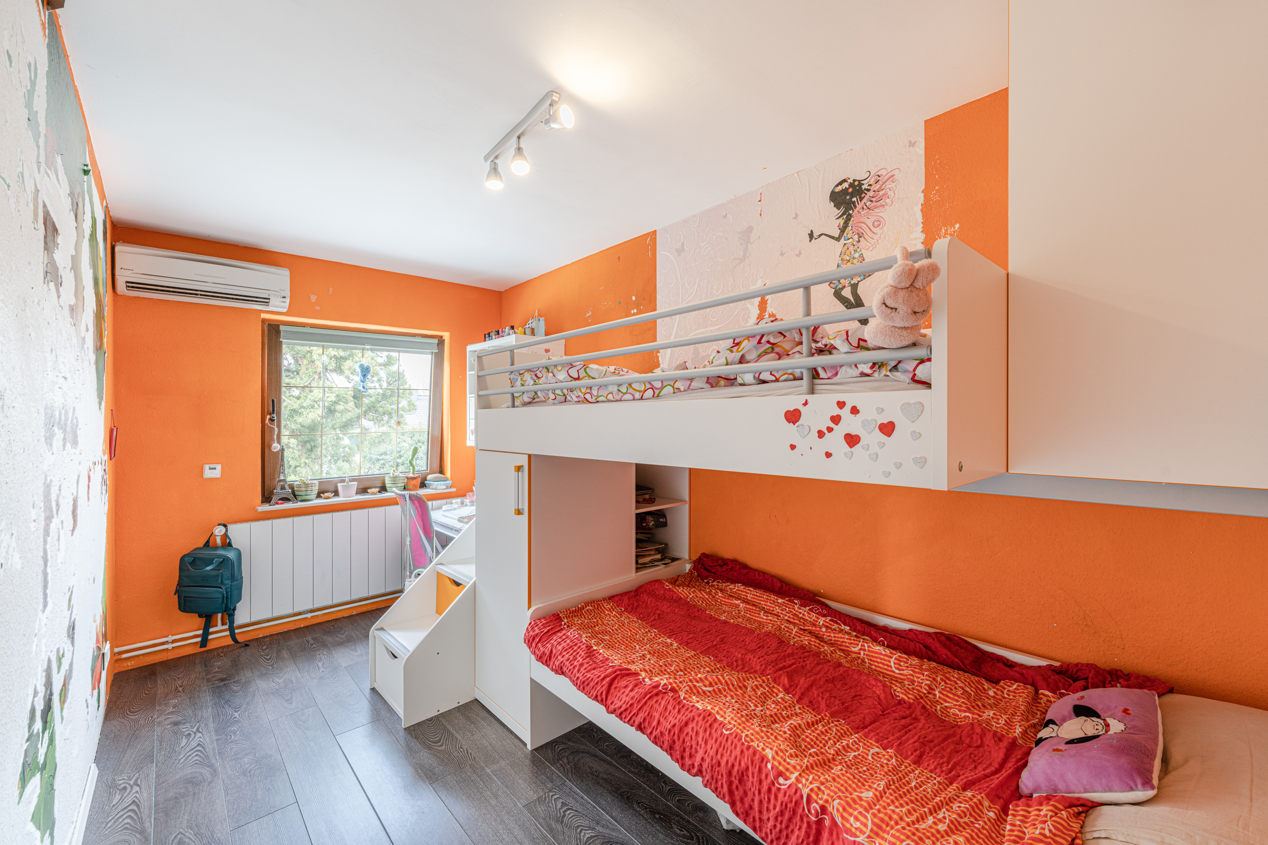 Kinderzimmer mit Etagenbett, orange Wand, Fenster und Schreibtisch unter dem Fenster.