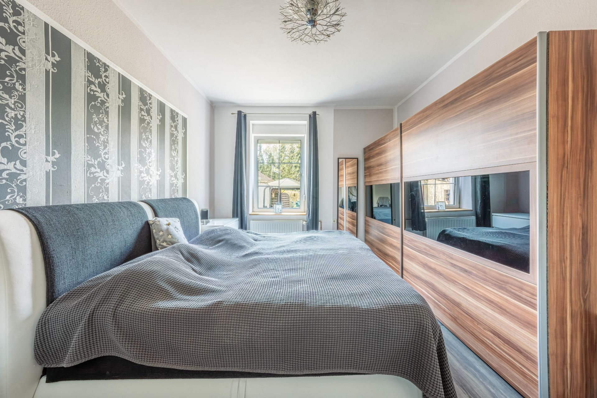 Modernes Schlafzimmer mit Doppelbett, großem Schrank und Fenster mit Blick nach draußen.