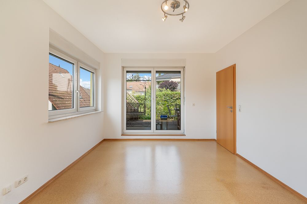 Helles, leeres Zimmer mit zwei Fenstern, Glastür zum Garten und Holztür rechts.