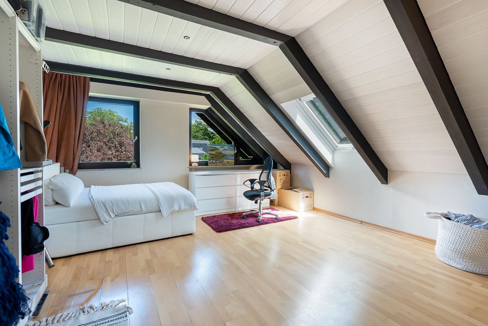 Helles Zimmer mit Dachschrägen, Bett, Schreibtisch und großen Fenstern, Holzboden.