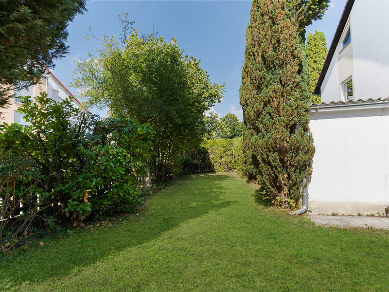 Garten mit grünem Rasen, Bäumen und einer weißen Hausfassade rechts.