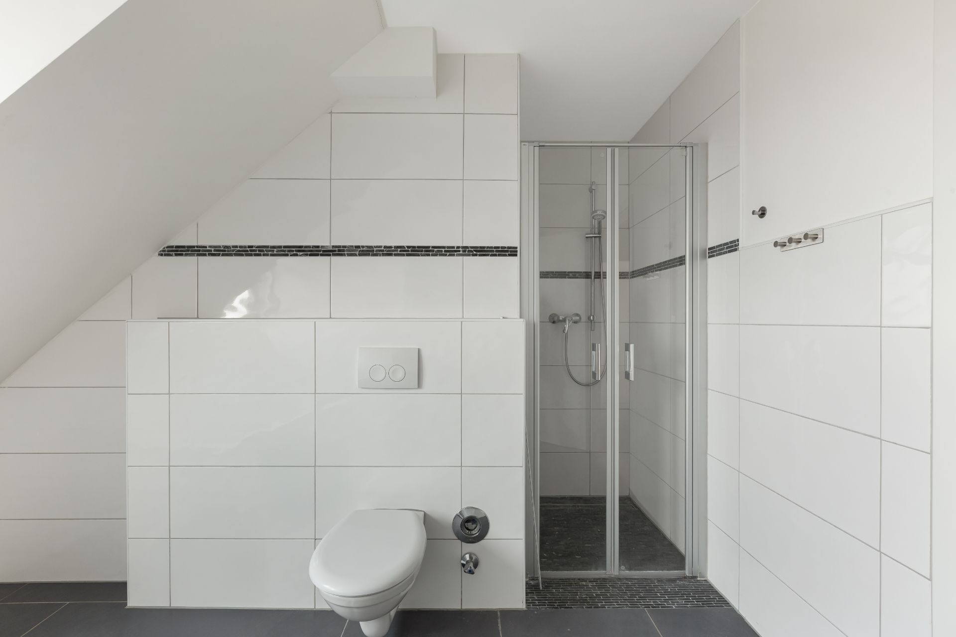 Modernes Badezimmer mit WC und verglaster Dusche unter einer Dachschräge.