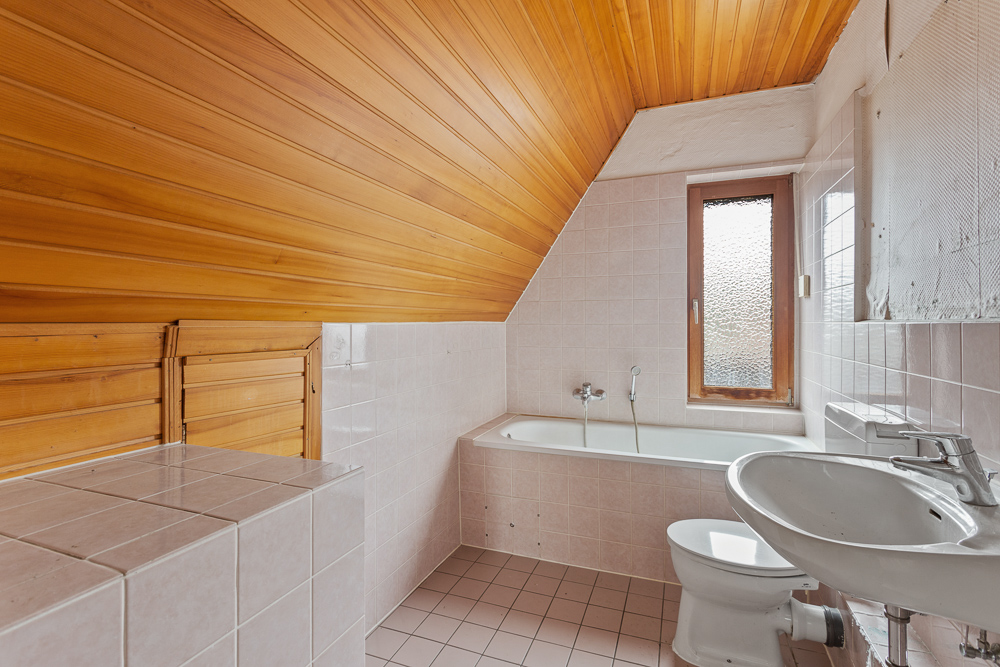 Badezimmer mit Badewanne, Waschbecken, Toilette und Holzdecke unter einer Dachschräge.