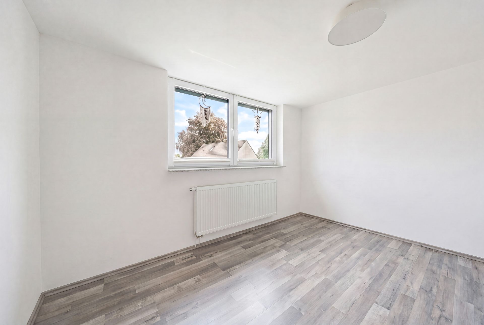 Leerer Raum mit hellem Laminatboden, weißen Wänden und großem Fenster.