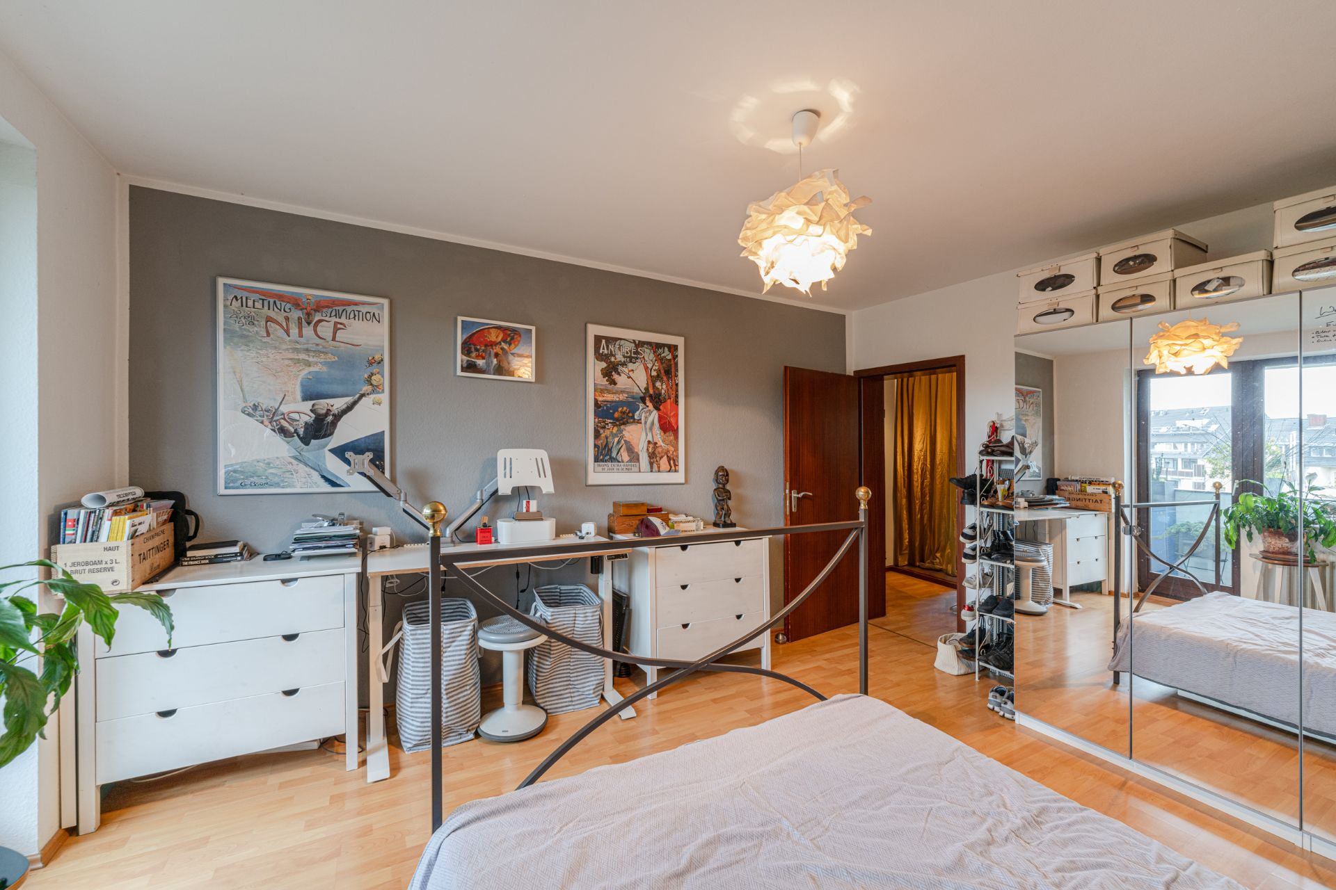 Helles Schlafzimmer mit Spiegel-Schrank, Bett, Schreibtisch und Dekoration an der Wand.