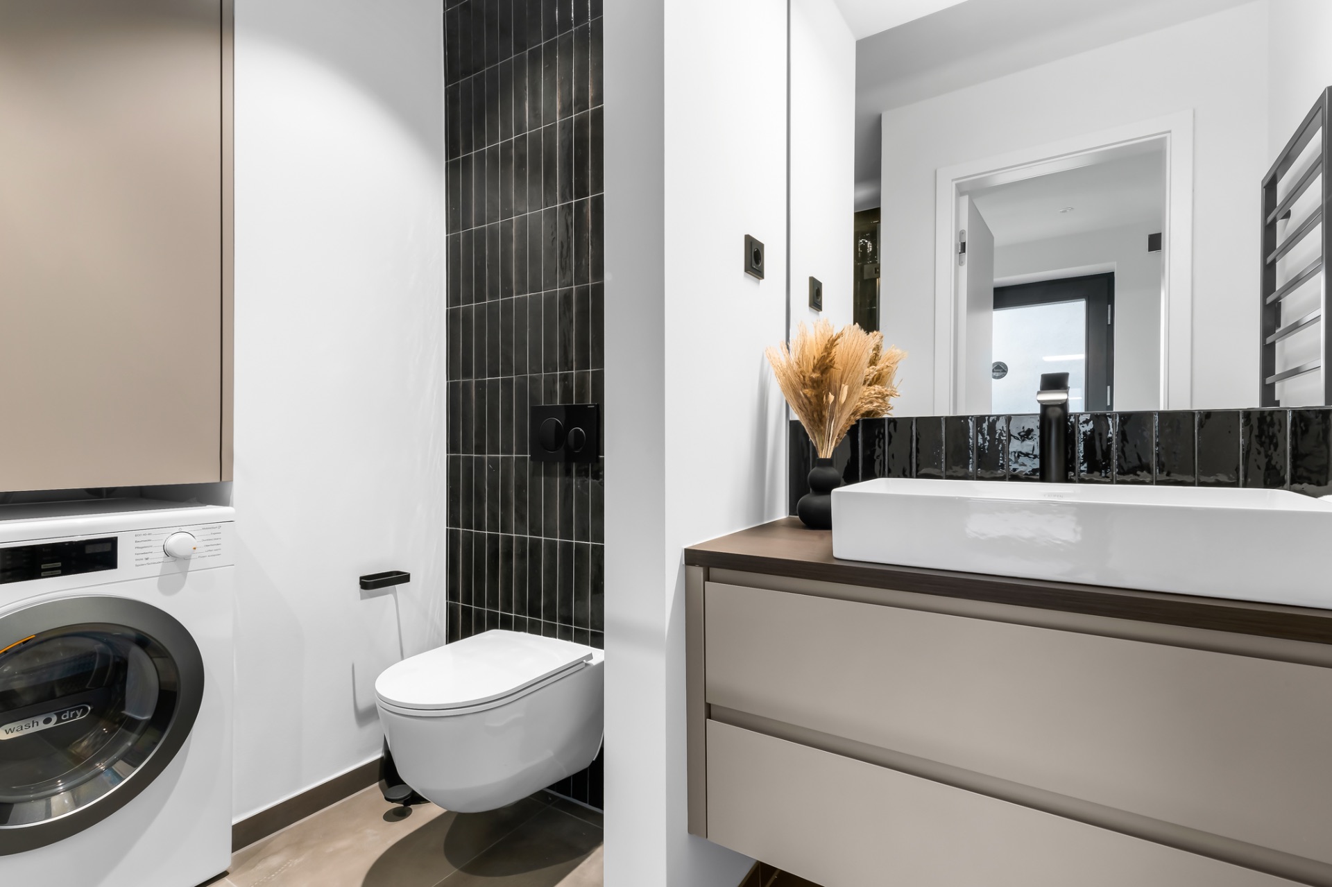 Modernes Badezimmer mit Waschbecken, Toilette, Waschmaschine und schwarzer Wandfliese.