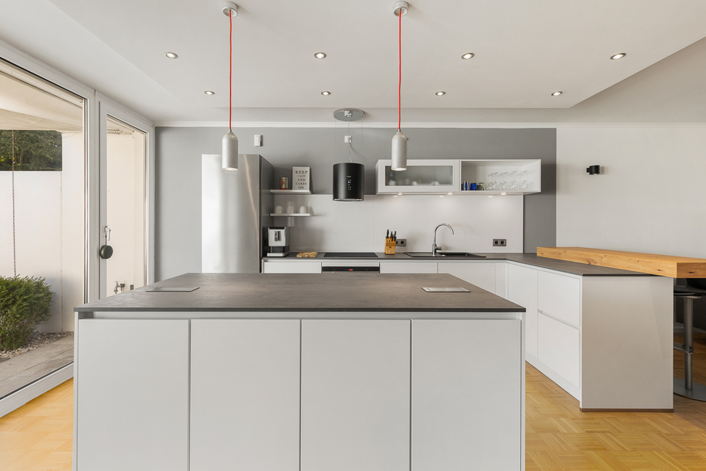 Moderne, helle Küche mit großer Kochinsel, weißen Schränken und Hängelampen.