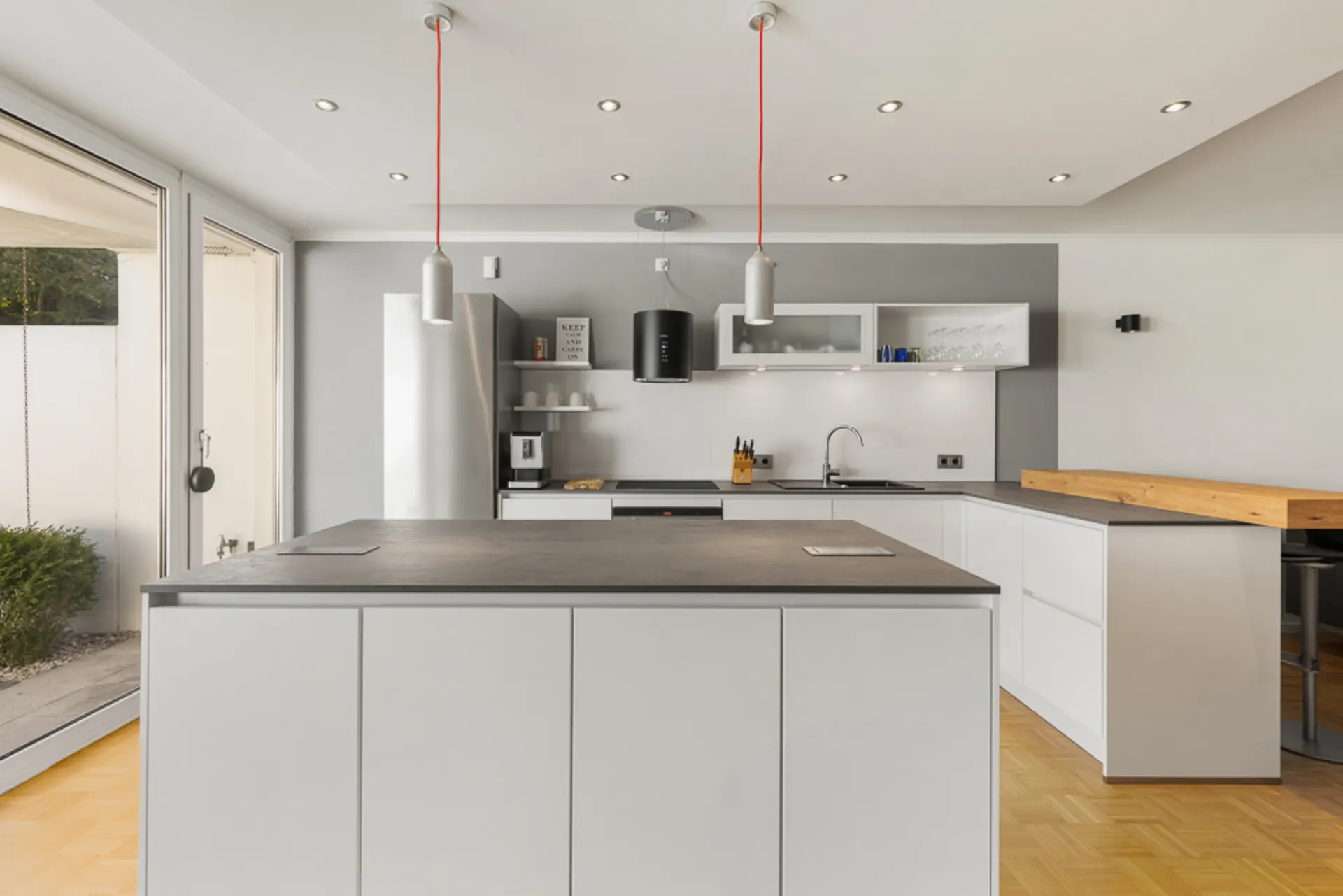 Moderne, helle Küche mit großer Kochinsel, weißen Schränken und Hängelampen.