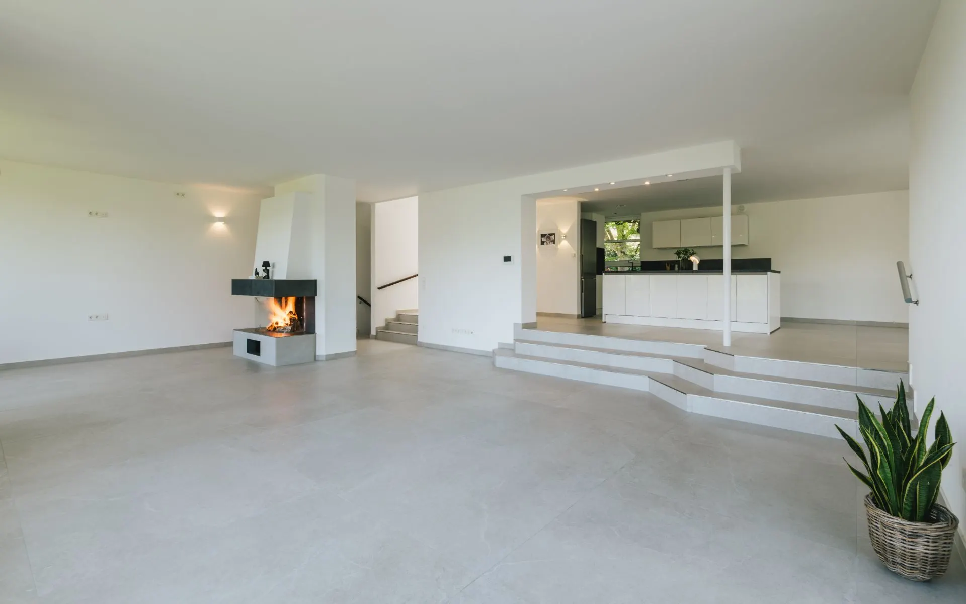 Großes, modernes Wohnzimmer mit Kamin, offener Küche, Treppe und Zimmerpflanze im Korb.