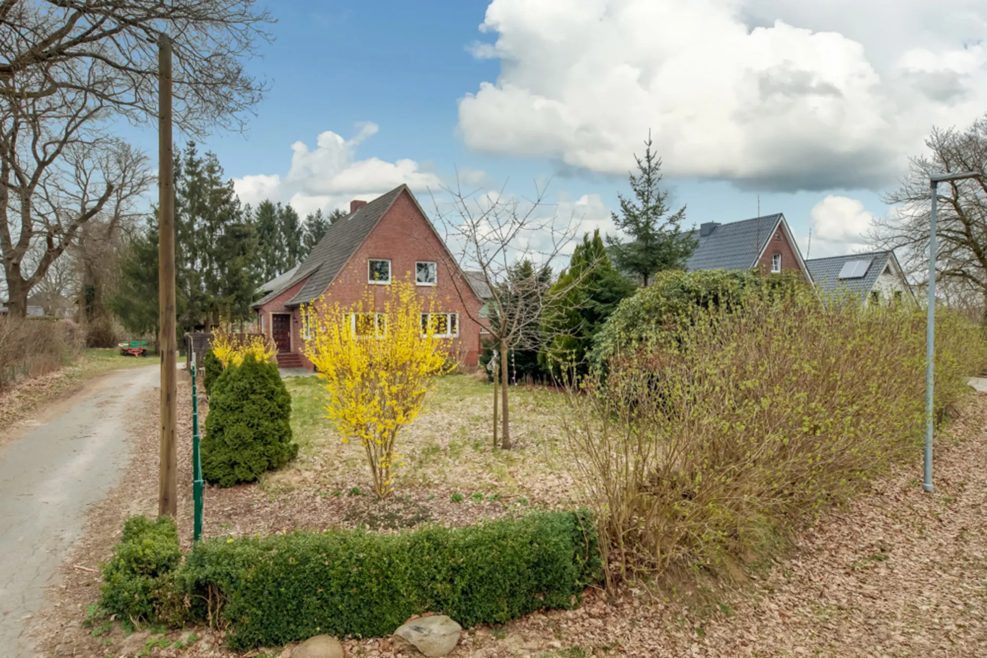 Backsteinhaus mit Garten und blühenden Sträuchern an einer kleinen Landstraße.