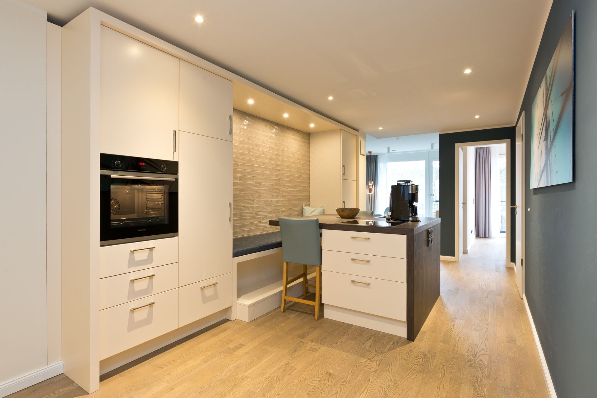 Moderne Küche mit weißen Schränken, Holzfußboden und Sitzbereich an der Arbeitsplatte.