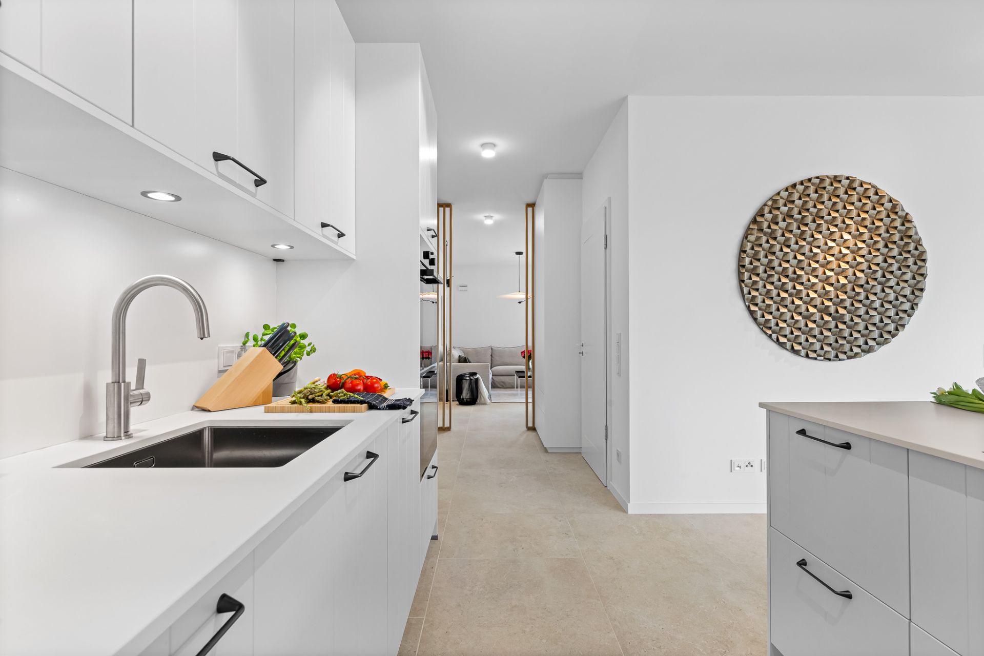Moderne weiße Küche mit Insel, Wanddekoration und Blick in einen offenen Wohnbereich.