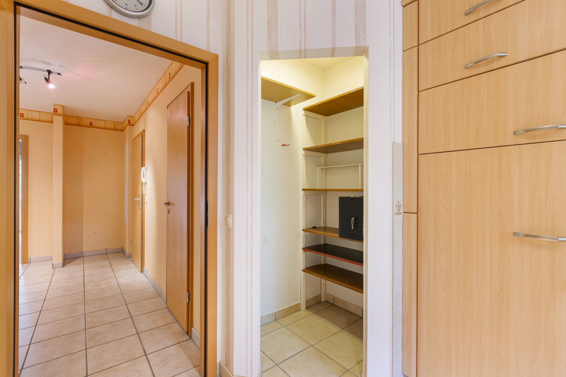 Flur mit Fliesenboden, offenem Einbauschrank und sichtbarem Safe auf einem Regal.