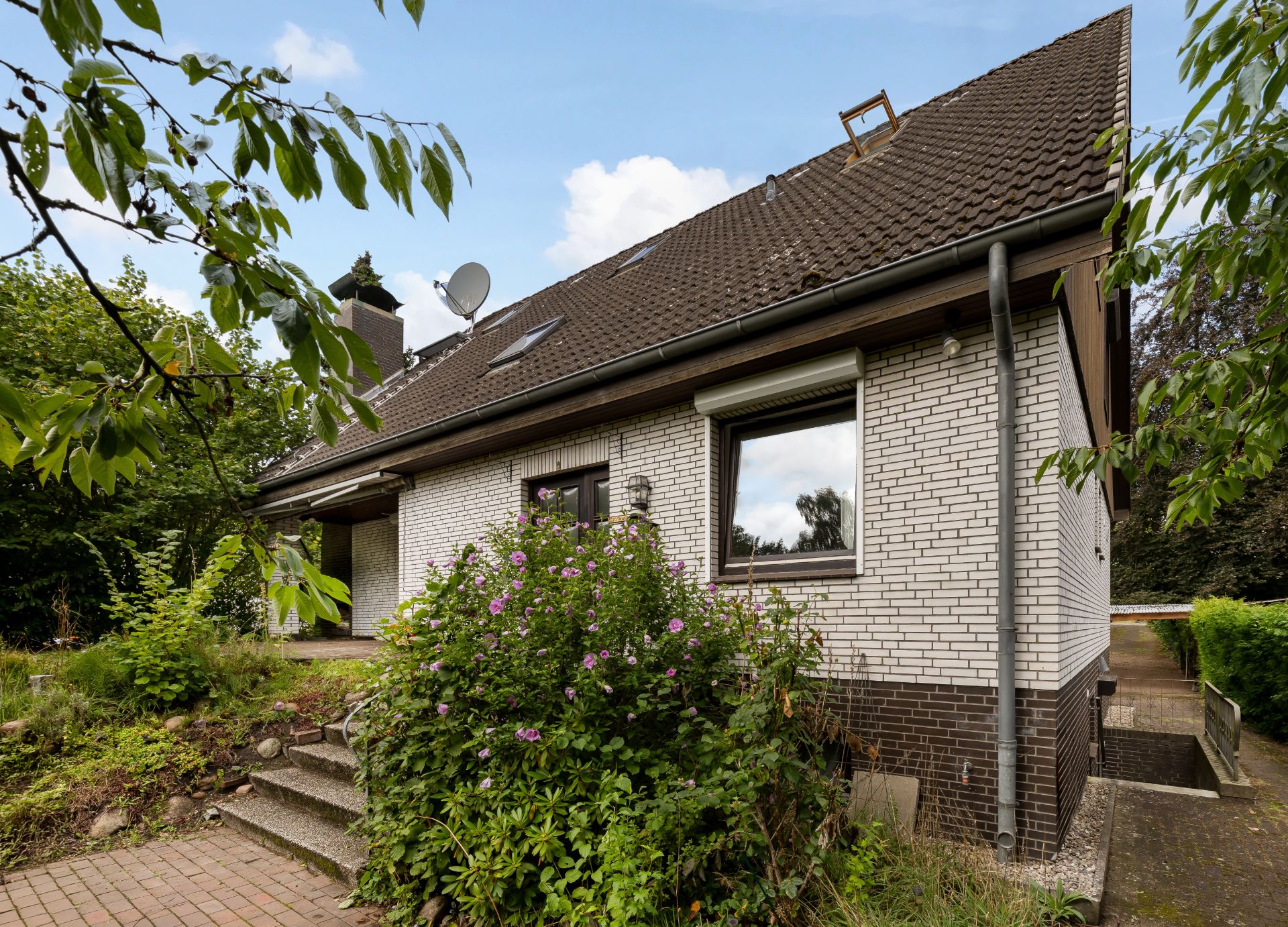 Einfamilienhaus mit Satteldach, weißen Klinkersteinen und Garten im Vordergrund.