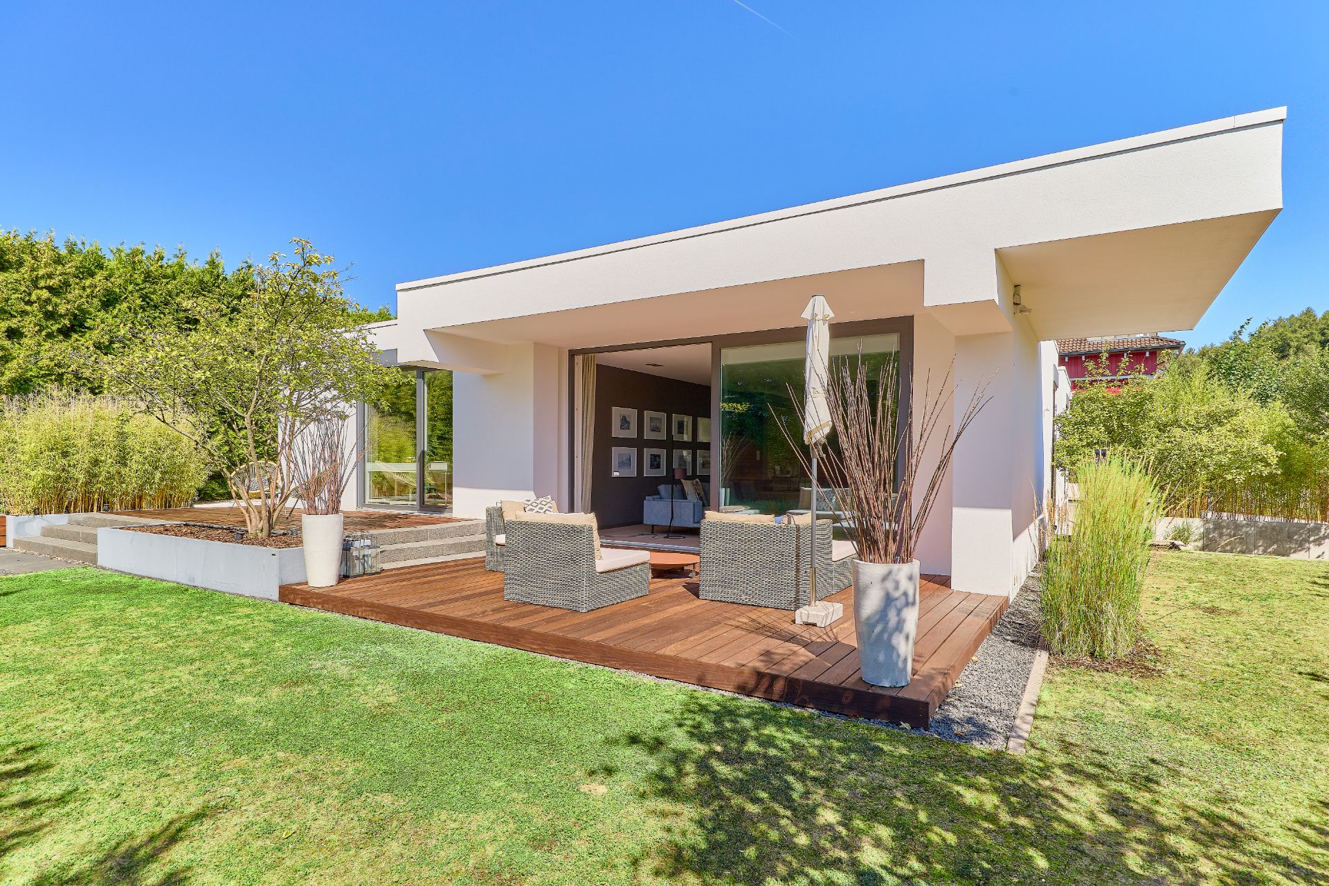 Moderne Terrasse mit Sitzmöbeln und Sonnenschirm an einem Einfamilienhaus mit Garten.