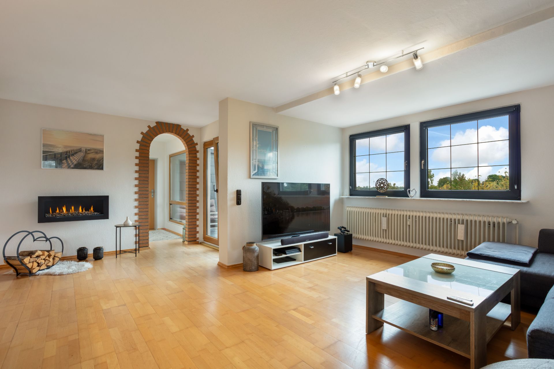 Modernes Wohnzimmer mit Sofa, Couchtisch, Fernseher, Kamin und großen Fenstern.
