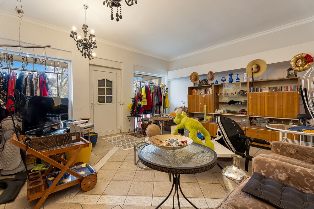 Wohnzimmer mit vielen Kleidern, Regalen, einem Tisch, Sofa und einem Fernseher.