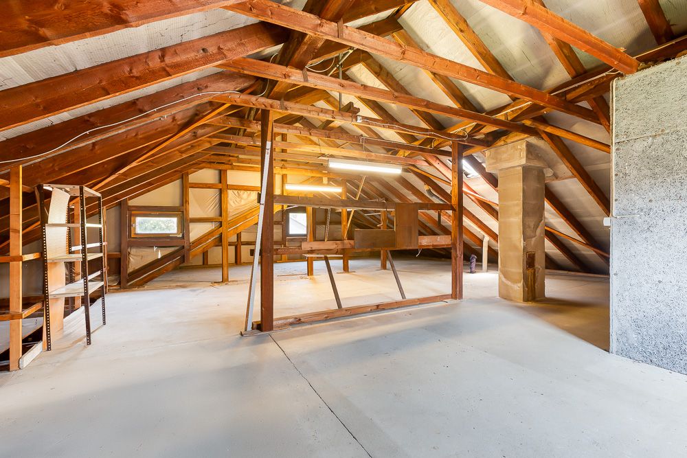 Heller, leerer Dachboden mit Holzbalken, Regalen und schrägen Fenstern.