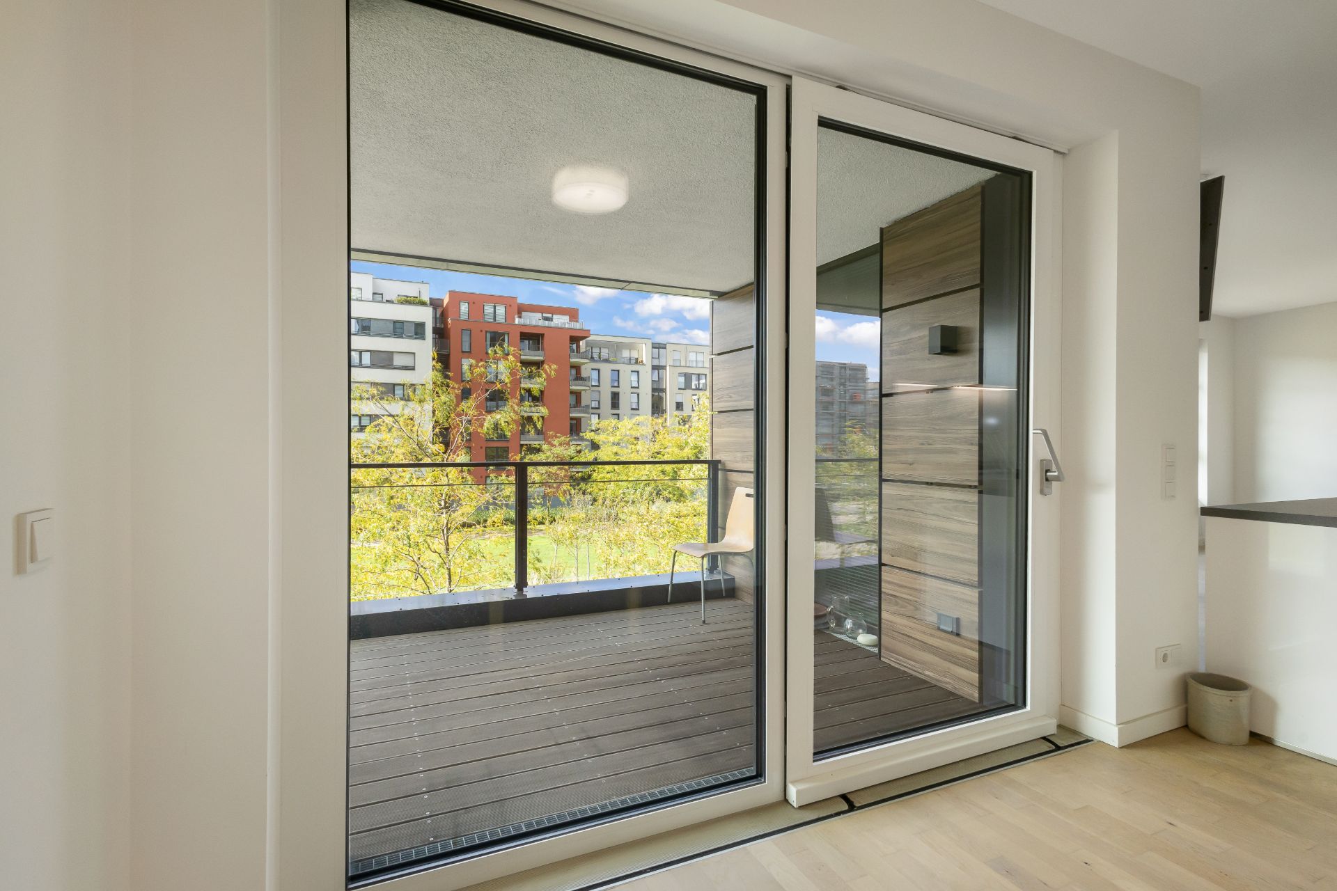 Große Glas-Schiebetür führt zu einem Balkon mit Blick auf moderne Wohngebäude und Bäume.