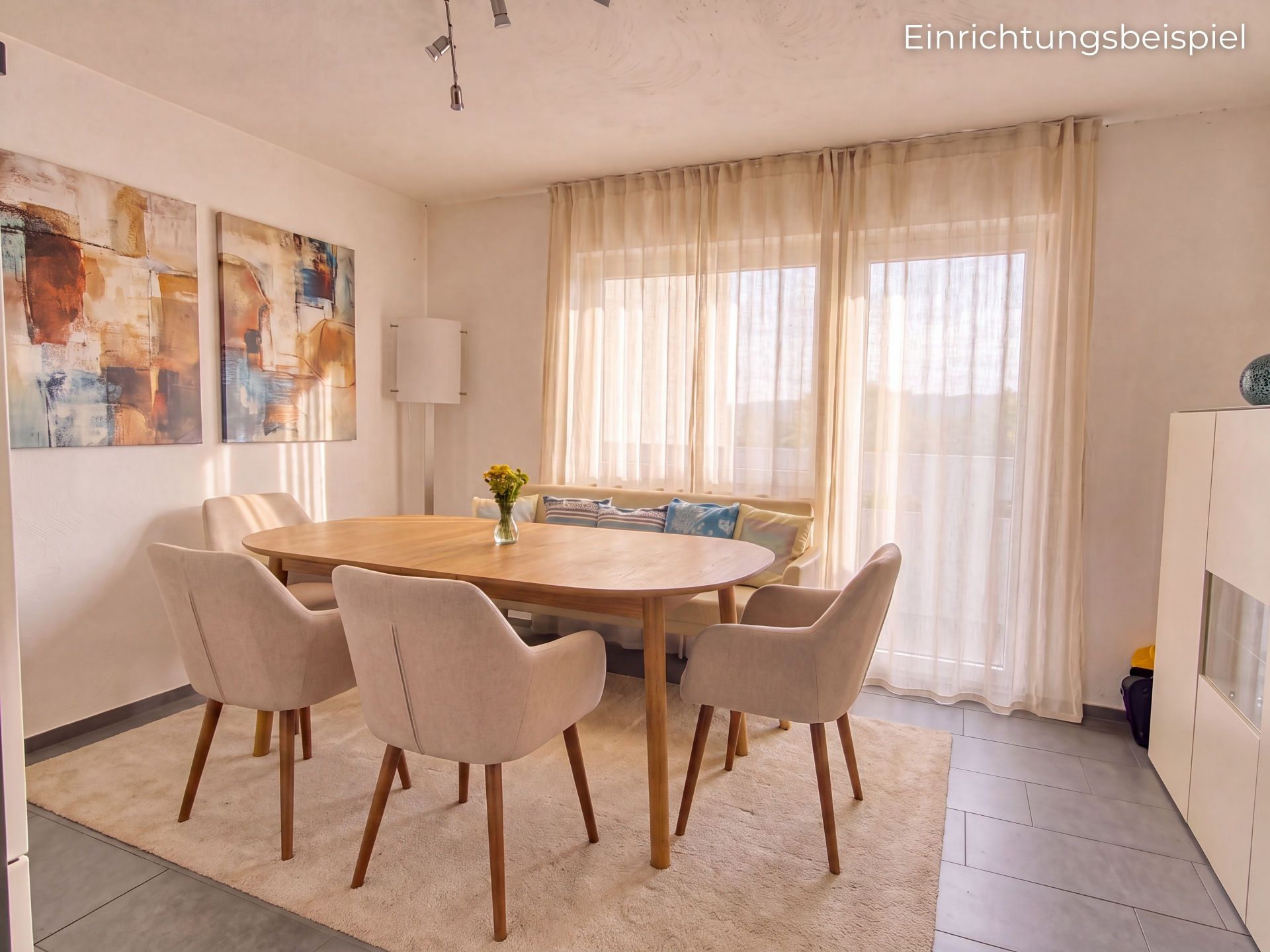 Esszimmer mit rundem Holztisch, fünf Stühlen, Gemälden an der Wand und großen Fenstern mit Vorhängen.