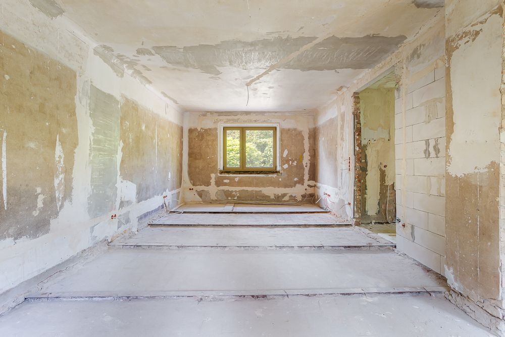 Ein leerer Raum im Rohbau mit unverputzten Wänden und einem Fenster am Ende.