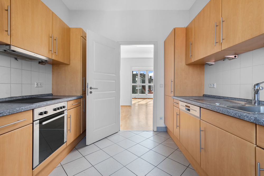 Moderne Einbauküche mit Holzmöbeln, Herd, Spüle und offen stehender Tür zum Wohnraum.
