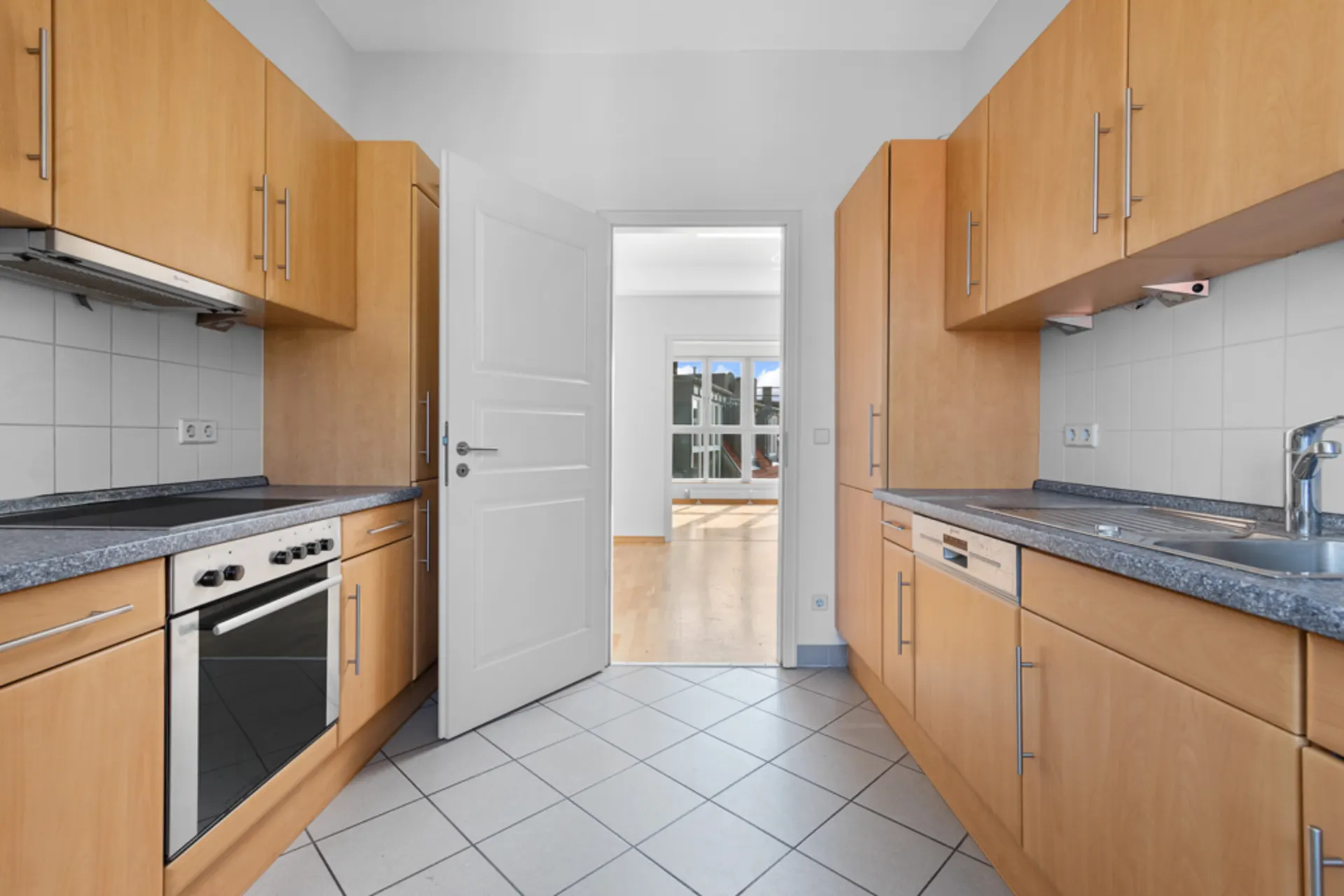 Moderne Einbauküche mit Holzmöbeln, Herd, Spüle und offen stehender Tür zum Wohnraum.