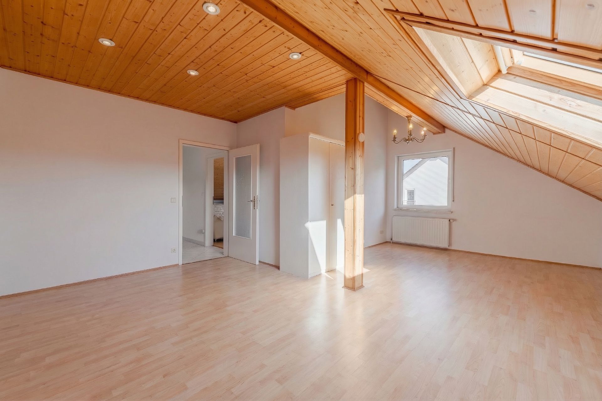 Helles Dachzimmer mit Holzdecke, Parkettboden, Fenster und Glastür.