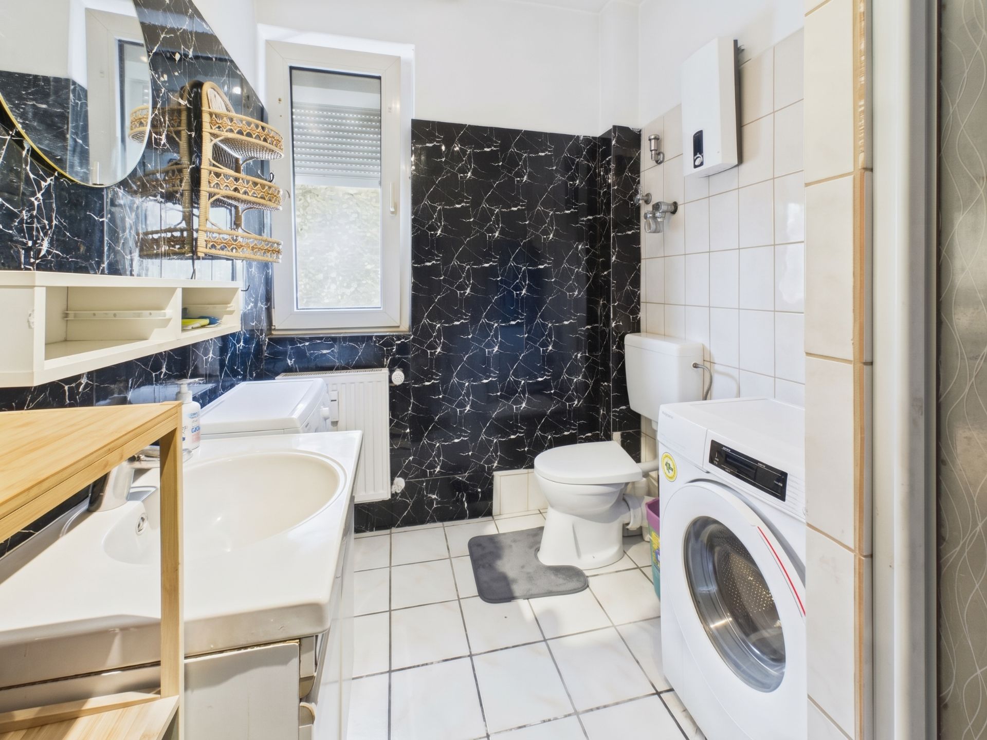 Helles Badezimmer mit Waschmaschine, WC, Waschbecken und Fenster, weiße Fliesen und dunkle Wandverkleidung.