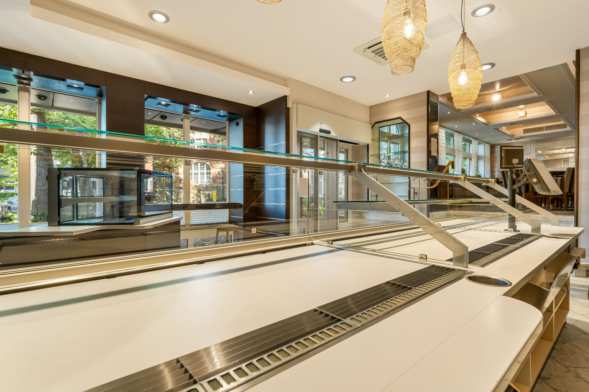 Leerer Speiseraum mit einer großen Buffettheke und Hängelampen, große Fenster im Hintergrund.