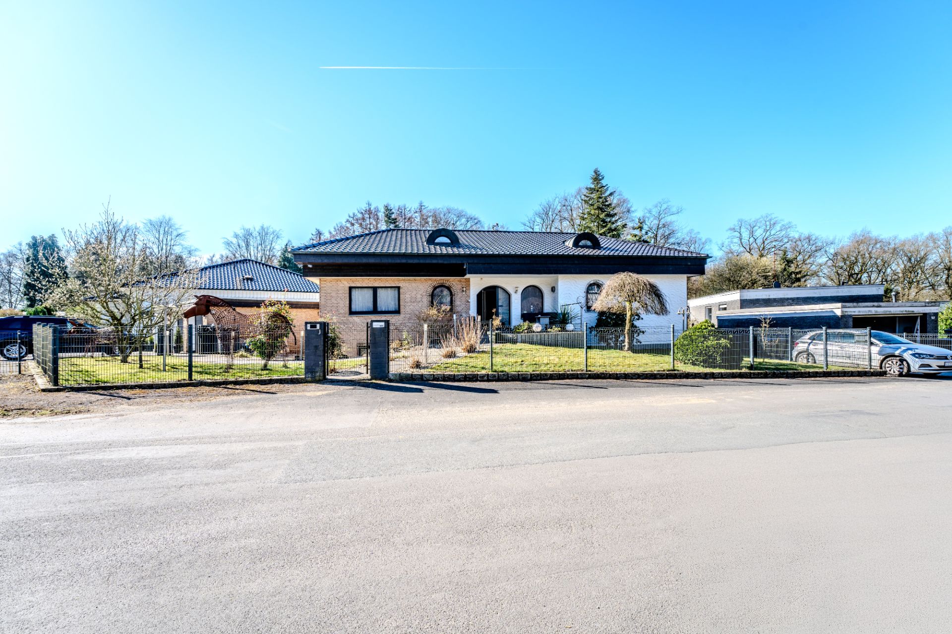 Einfamilienhaus mit Garten und Zaun, aufgenommen von der Straße bei klarem Wetter.